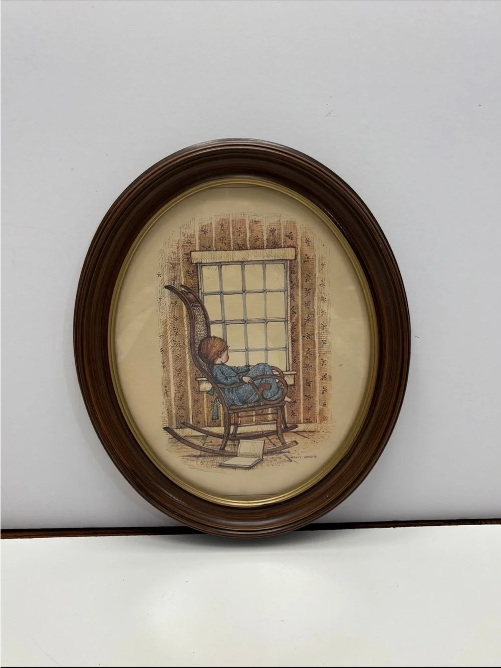Vintage oval framed wall art piece featuring a girl in a rocking chair by a wind